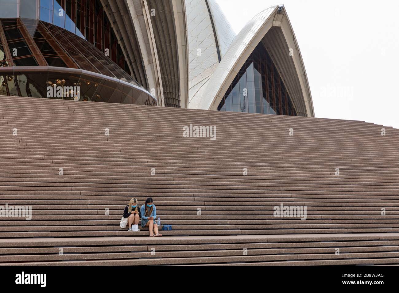 Sydney Opera House, Australia. Lunedì 23 Marzo 2020. Abbandonate le due ragazze asiatiche che indossano i maks del viso e che giocano con i loro telefoni sui gradini dell'Opera House. Credit Martin Berry/Alamy Live News Foto Stock