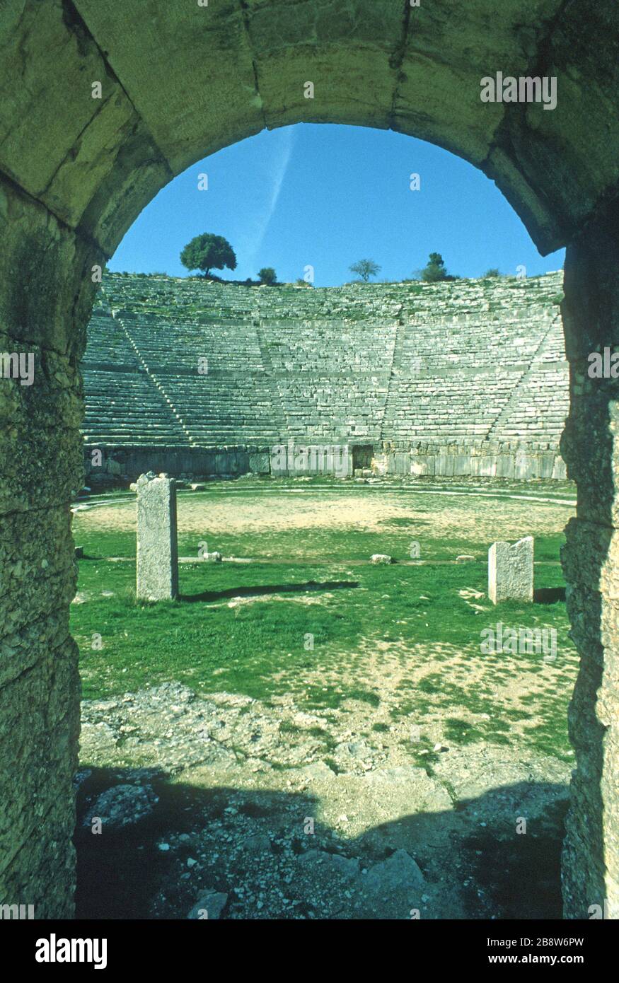 L'antico teatro greco di Dodoni, Ioannina, Epiro, Grecia, visto dall'ingresso degli artisti, mostra file curve di sedili in pietra che guardano verso il basso sul palcoscenico e scalano fino ad ogni livello. Cielo blu sullo sfondo. Dodoni è uno dei 15 teatri dell'antica Grecia, con lo status di patrimonio dell'umanità dell'UNESCO. Foto Stock