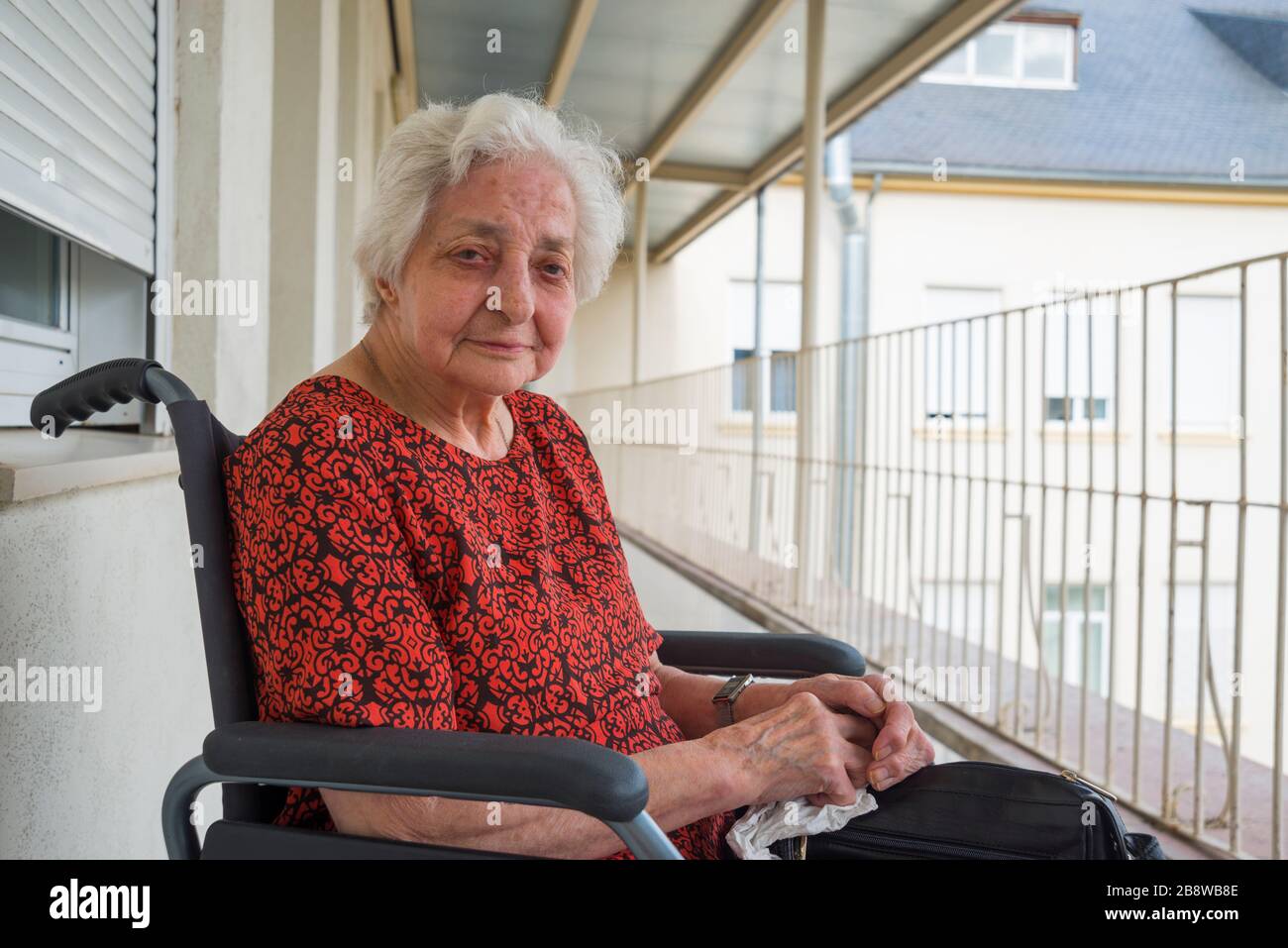 Vecchia signora seduta in una terrazza di una casa di cura, sorridente e guardando la macchina fotografica. Foto Stock
