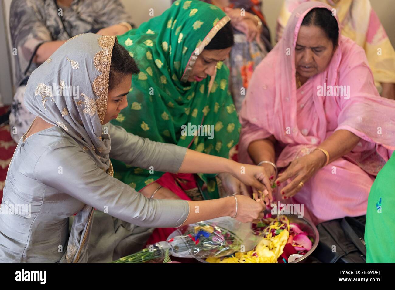 Devout Sikh donne di diverse età rompere di petali di fiori da utilizzare in un servizio mattutino. Al Centro Culturale Sikh a South Richmond Hill, Queens. Foto Stock