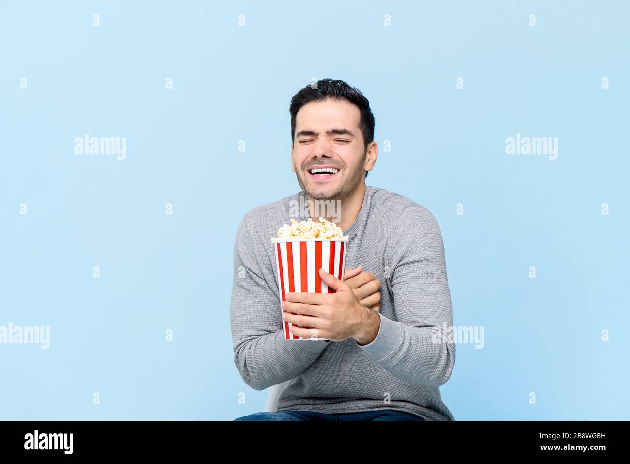 Giovane uomo che tiene pop corn ridere mentre guarda il film isolato su sfondo blu chiaro Foto Stock