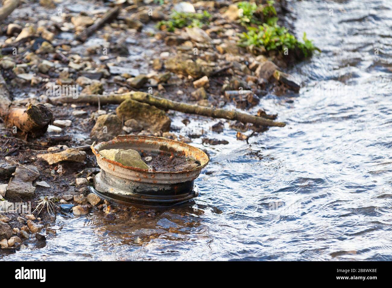 Primo piano di un cerchio di auto arrugginito abbandonato su una riva del fiume. Foto Stock