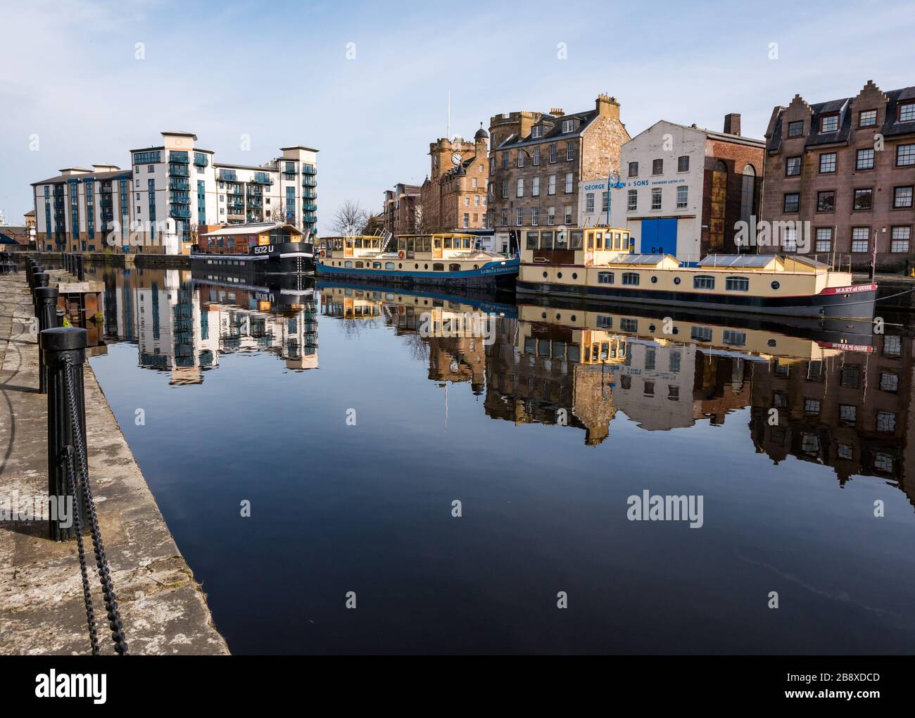 The Shore, Leith, Edimburgo, Scozia, Regno Unito. 23 marzo 2020. UK Weather: Il sole primaverile e la brezza creano un perfetto riflesso dei vecchi edifici e chiatte nell'acqua di Leith lungo la riva deserta del fiume, mentre la gente rimane a casa a distanza sociale Foto Stock