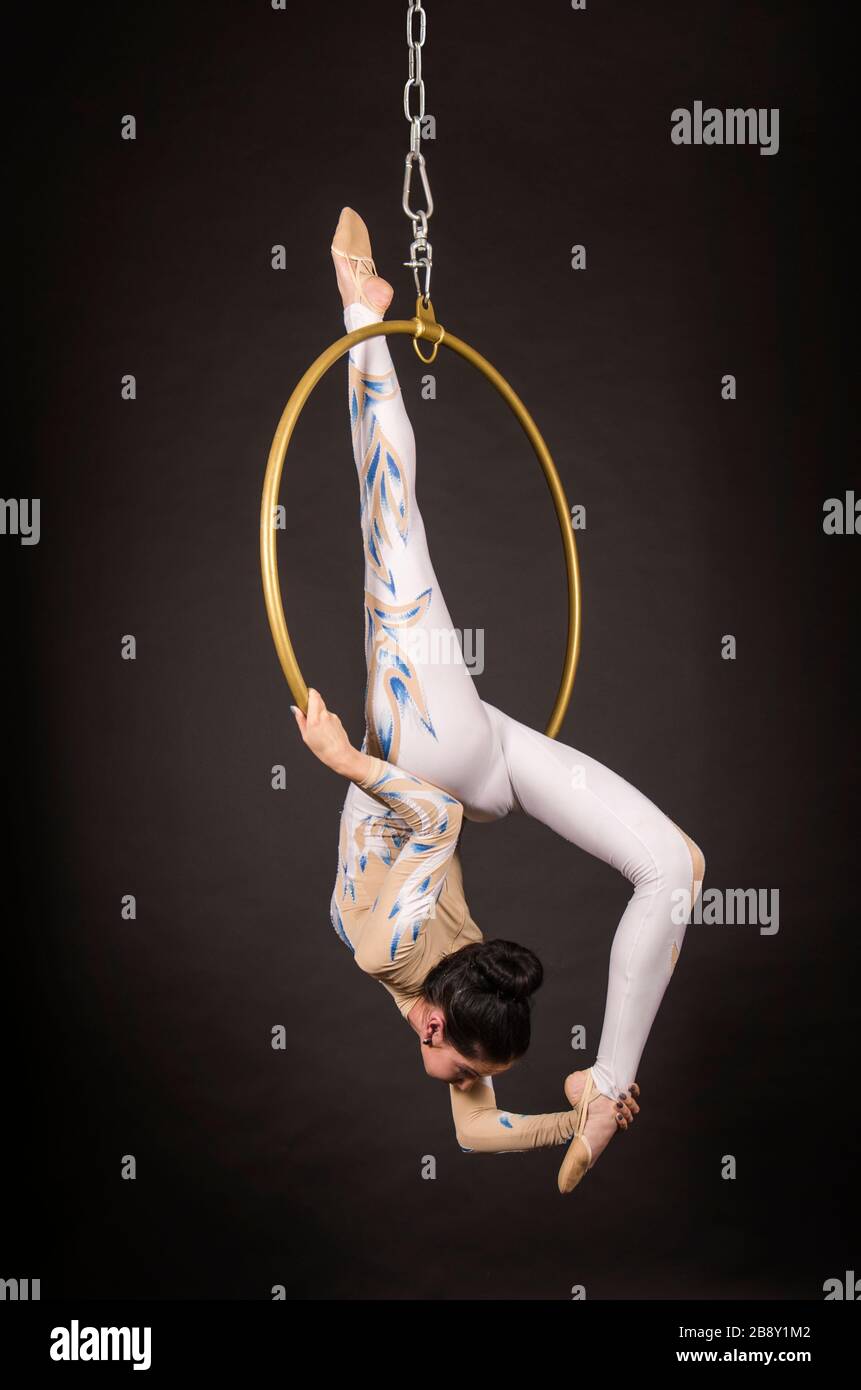Una donna snella, dai capelli scuri - un acrobata d'aria in un vestito bianco e blu, esegue esercizi in un anello d'aria. Riprese in studio su sfondo scuro. Foto Stock