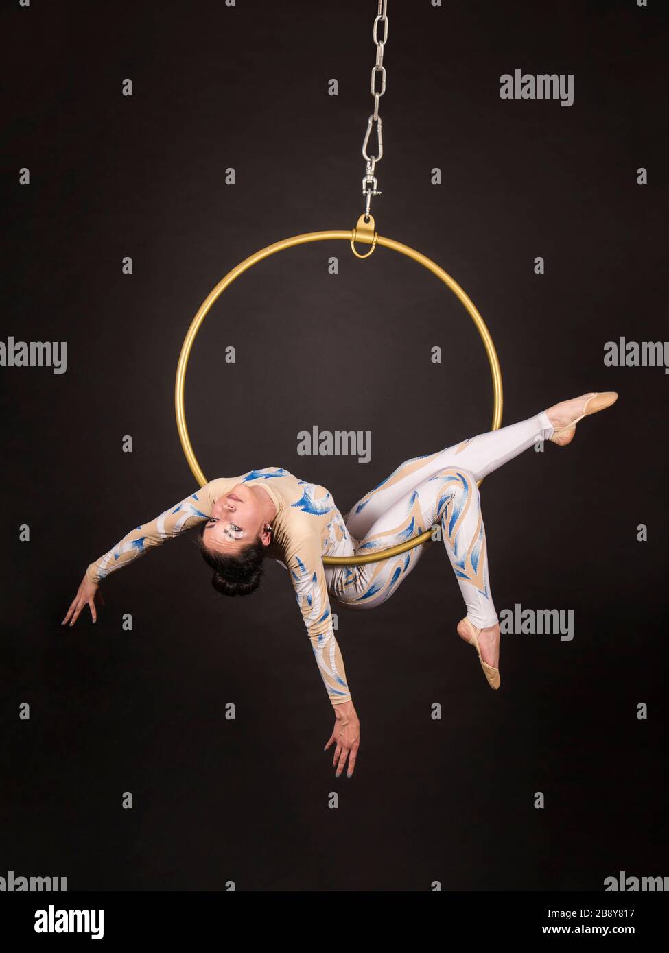 Una donna snella, dai capelli scuri - un acrobata d'aria in un vestito bianco e blu, esegue esercizi in un anello d'aria. Riprese in studio su sfondo scuro. Foto Stock
