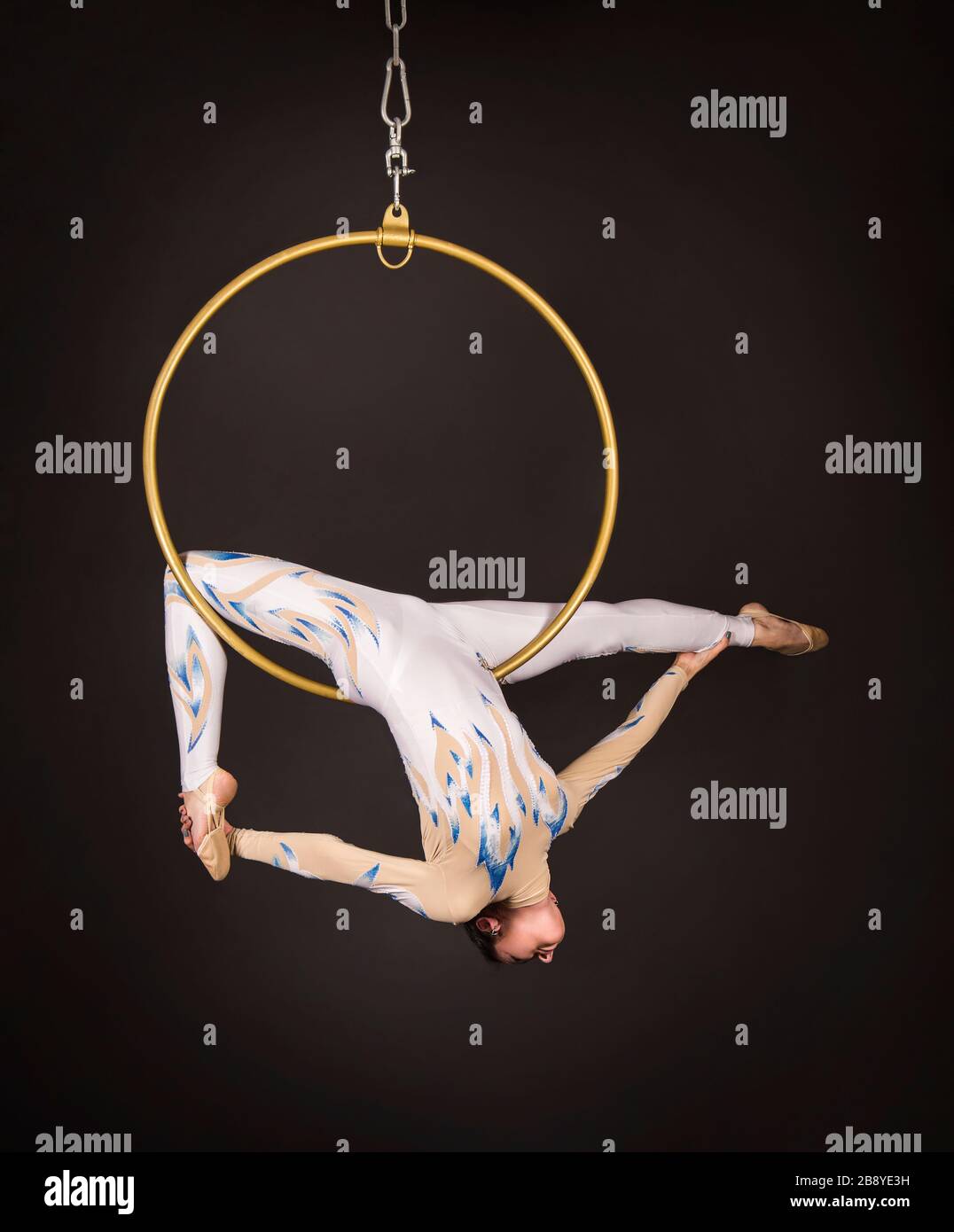 Una donna snella, dai capelli scuri - un acrobata d'aria in un vestito bianco e blu, esegue esercizi in un anello d'aria. Riprese in studio su sfondo scuro. Foto Stock