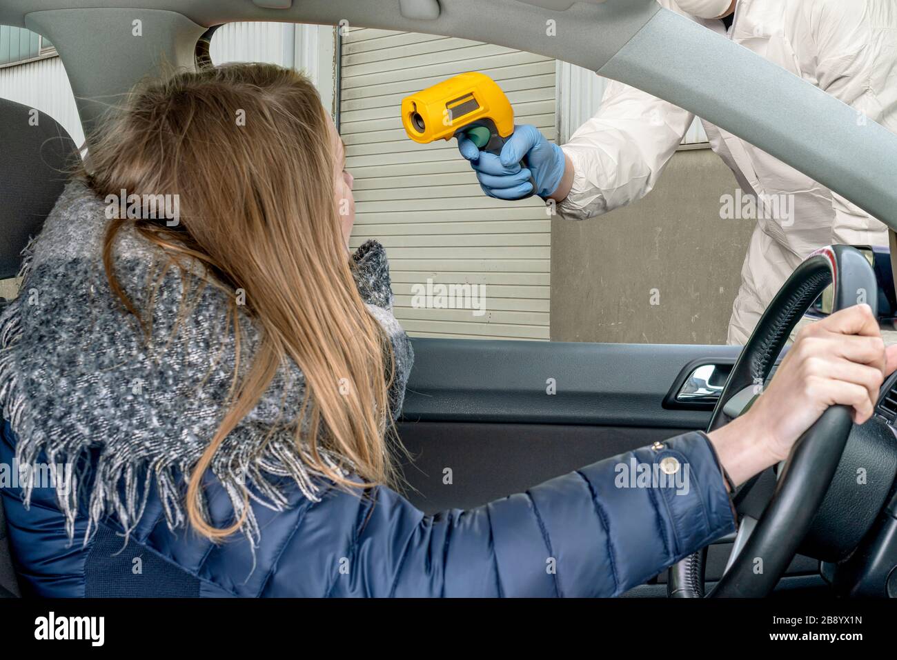 una persona in tuta di protezione controlla la temperatura di una guida femmina Foto Stock