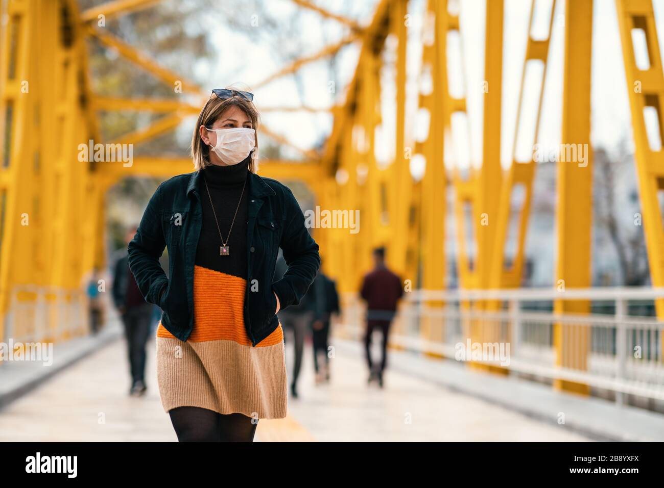 Una giovane donna sconsiderata cammina su strade affollate con una maschera in un periodo di quarantena a causa di pandemico pericolo globale Foto Stock