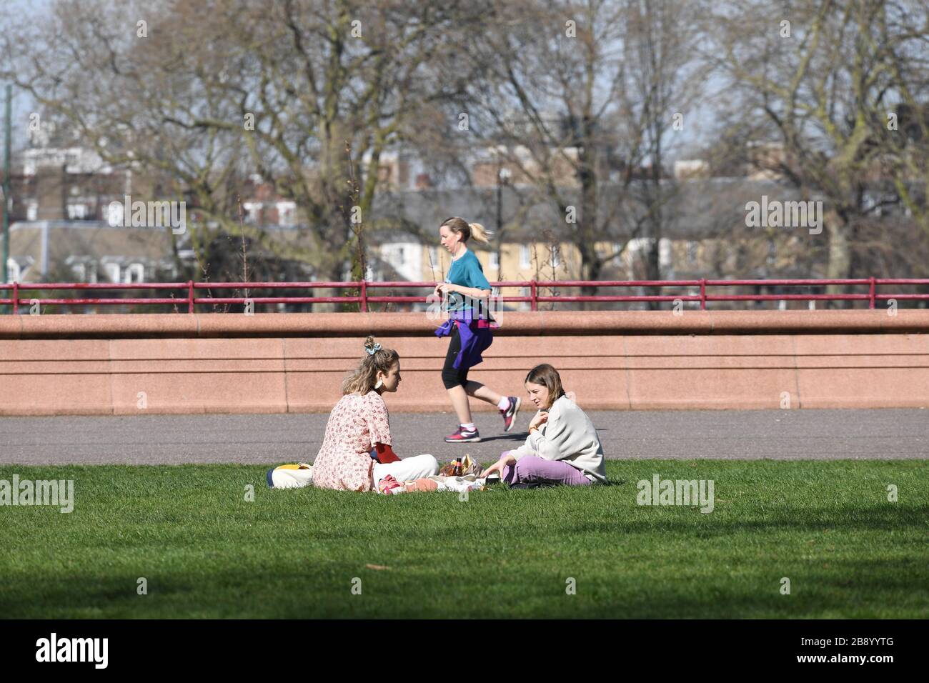 Una donna scherza davanti a due donne che socializzano a Battersea Park, Londra, come ha detto il primo ministro Boris Johnson, il governo è pronto ad imporre restrizioni più severe per frenare la diffusione del coronavirus se la gente non segue le linee guida sulle distanze sociali. Foto Stock
