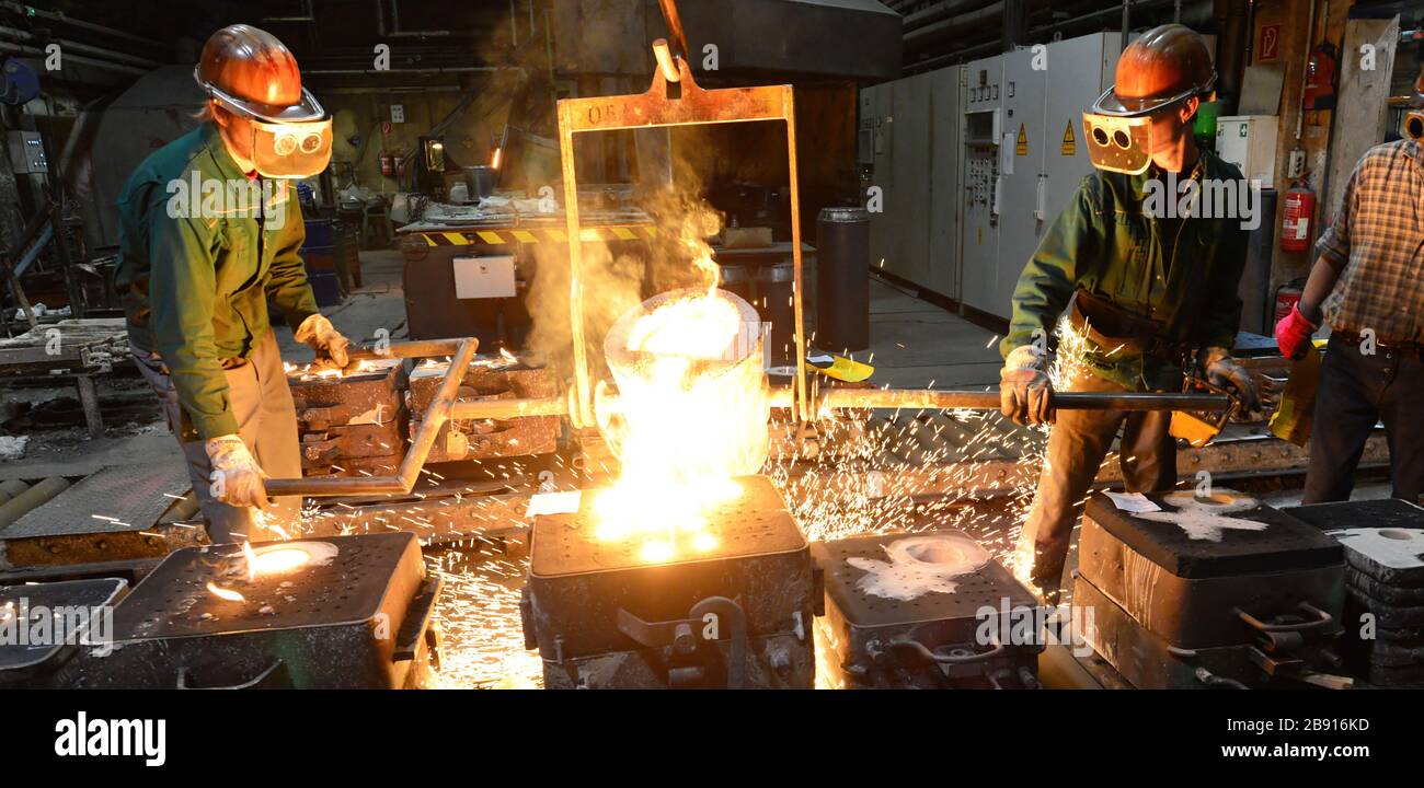 I lavoratori in un getto di fonderia di un pezzo di metallo - Sicurezza sul lavoro e il lavoro di squadra Foto Stock