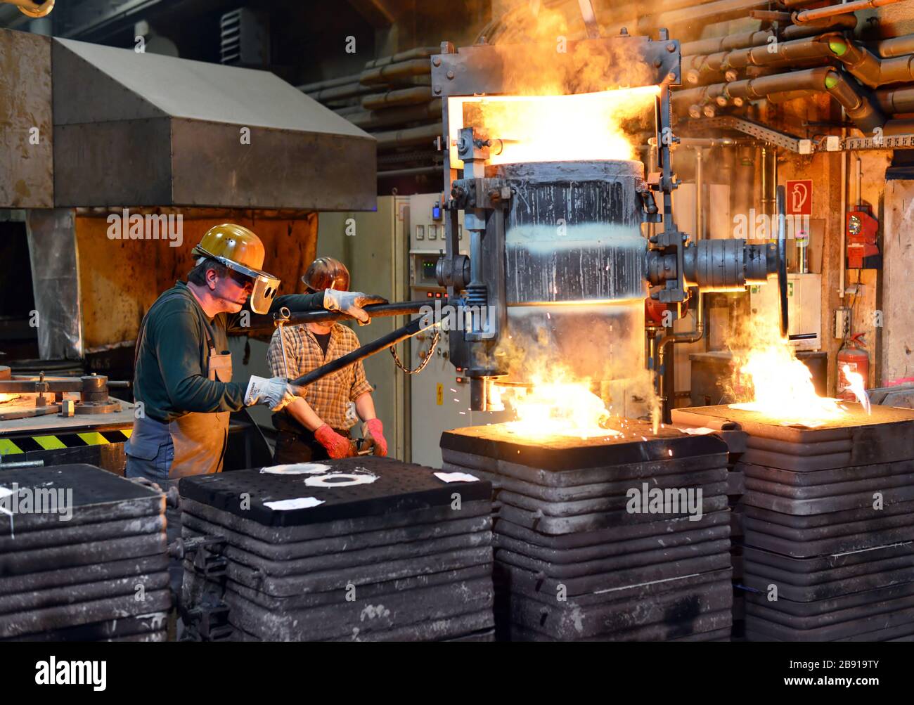 I lavoratori in un getto di fonderia di un pezzo di metallo - Sicurezza sul lavoro e il lavoro di squadra Foto Stock