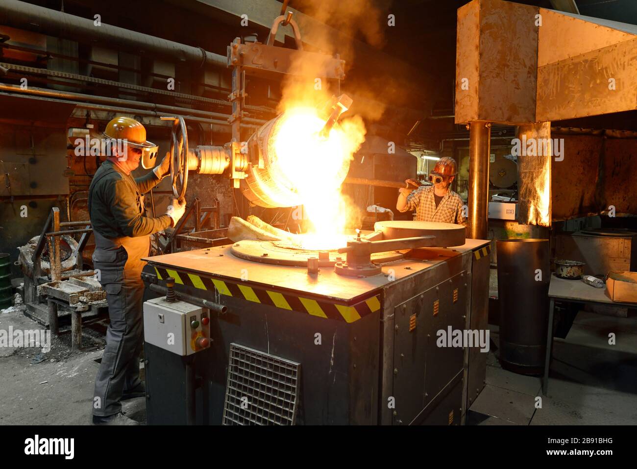 I lavoratori in un getto di fonderia di un pezzo di metallo - Sicurezza sul lavoro e il lavoro di squadra Foto Stock