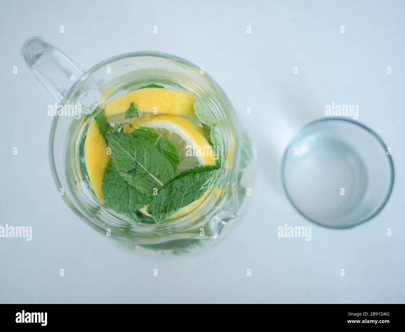 vista dall'alto sulla caraffa di limonata fatta in casa con foglie di menta e fette di limone o cunei di lime e tazza di vetro. Foto Stock