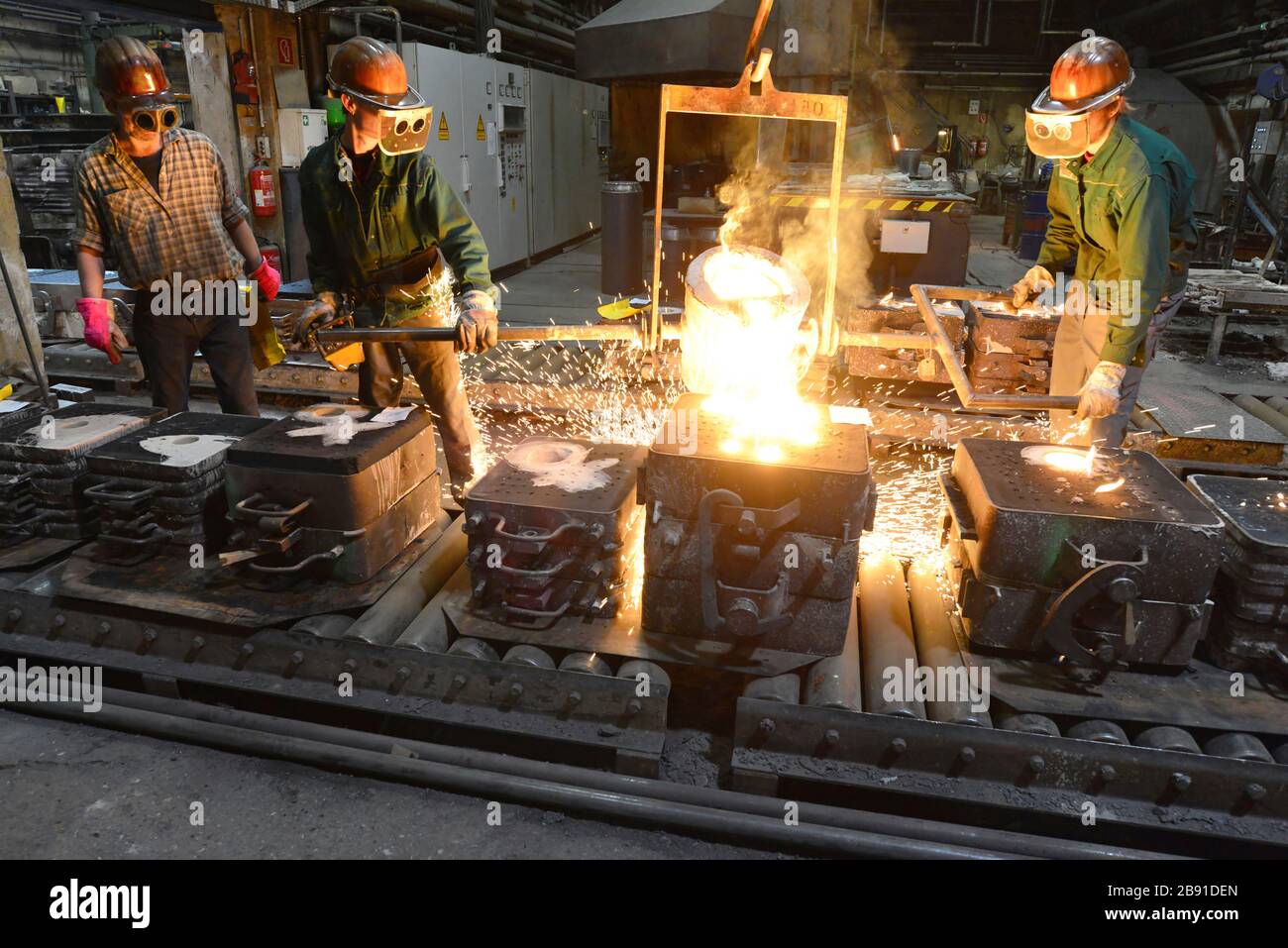 I lavoratori in un getto di fonderia di un pezzo di metallo - Sicurezza sul lavoro e il lavoro di squadra Foto Stock