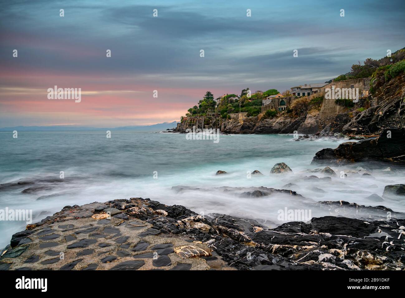 Tramonto lungo la costa a Bogliasco, Golfo Paradiso, Liguria, Italia con una vista lontana su un promontorio roccioso con edifici e un bagliore rosa sul Foto Stock