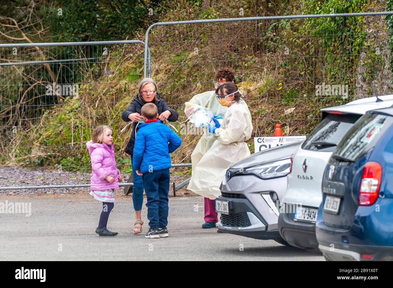 Dunmanway, West Cork, Irlanda. 23 Marzo 2020. Dunmanway Community Hospital sta attualmente gestando un centro di test di emergenza Coronavirus. Una madre mette una maschera protettiva su un ragazzo prima di entrare nel centro di test COVID-19 mentre due operatori ospedalieri guardano. Credit: Notizie dal vivo di AG/Alamy Foto Stock