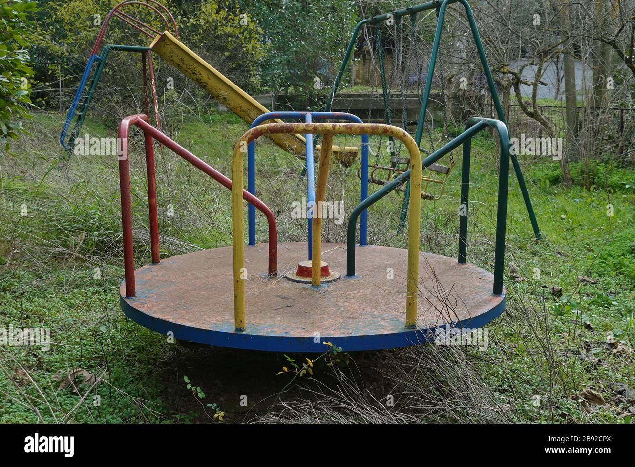 Parco giochi nel giardino sovrastato di una casa abbandonata. Arrugginita altalene e scivoli. Foto Stock