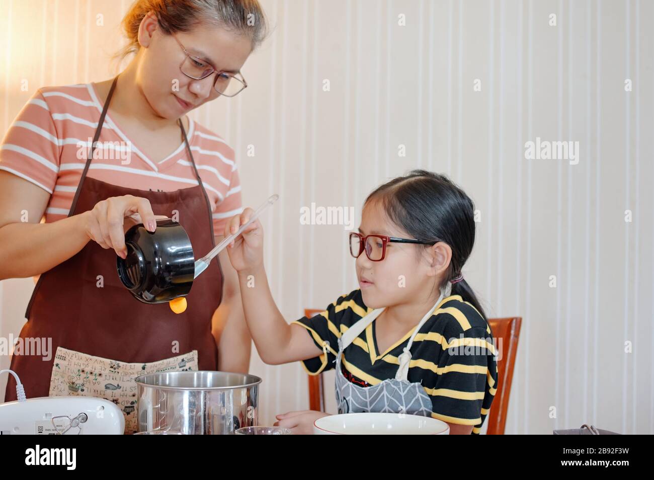 Madre e figlia aggiungere il tuorlo alla ciotola di miscelazione Foto Stock