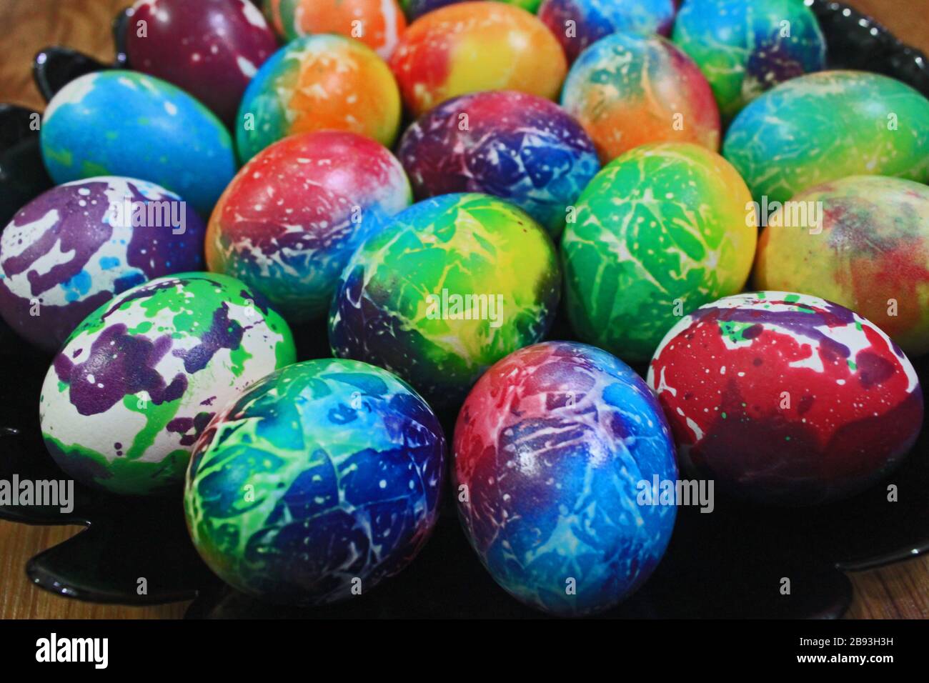 Uova di Pasqua colorate su piatto nero su sfondo di legno Foto Stock