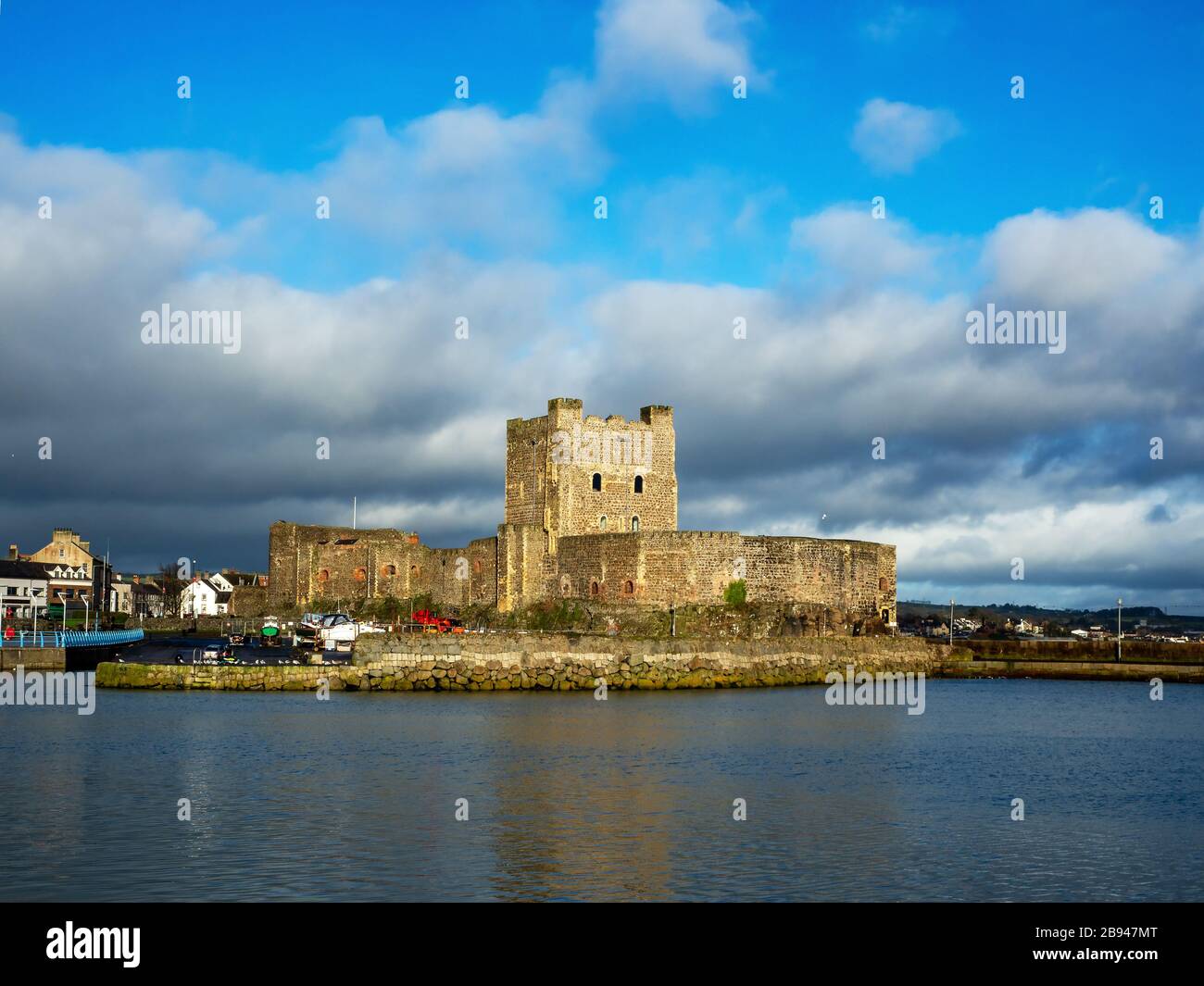 Castello Normanno medievale a Carrickfergus vicino a Belfast, Irlanda del Nord, con marina in inverno. Cielo drammatico con nuvole tempestose scure. Luce del tramonto Foto Stock