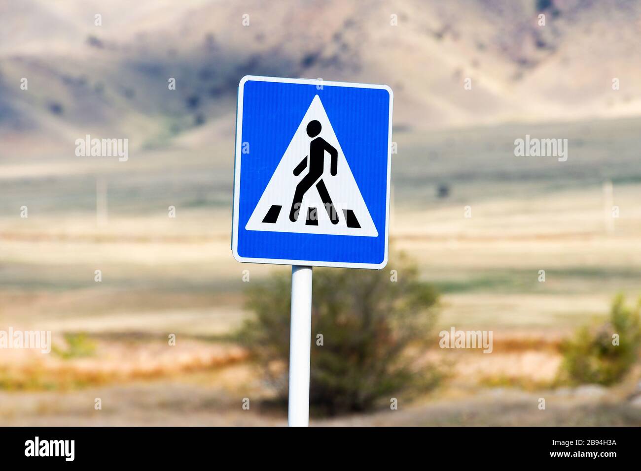 Cartello bianco e blu che indica una persona che attraversa la passerella in sicurezza. Segnale stradale con sfondo di montagne fuori fuoco in Kirghizistan, Foto Stock