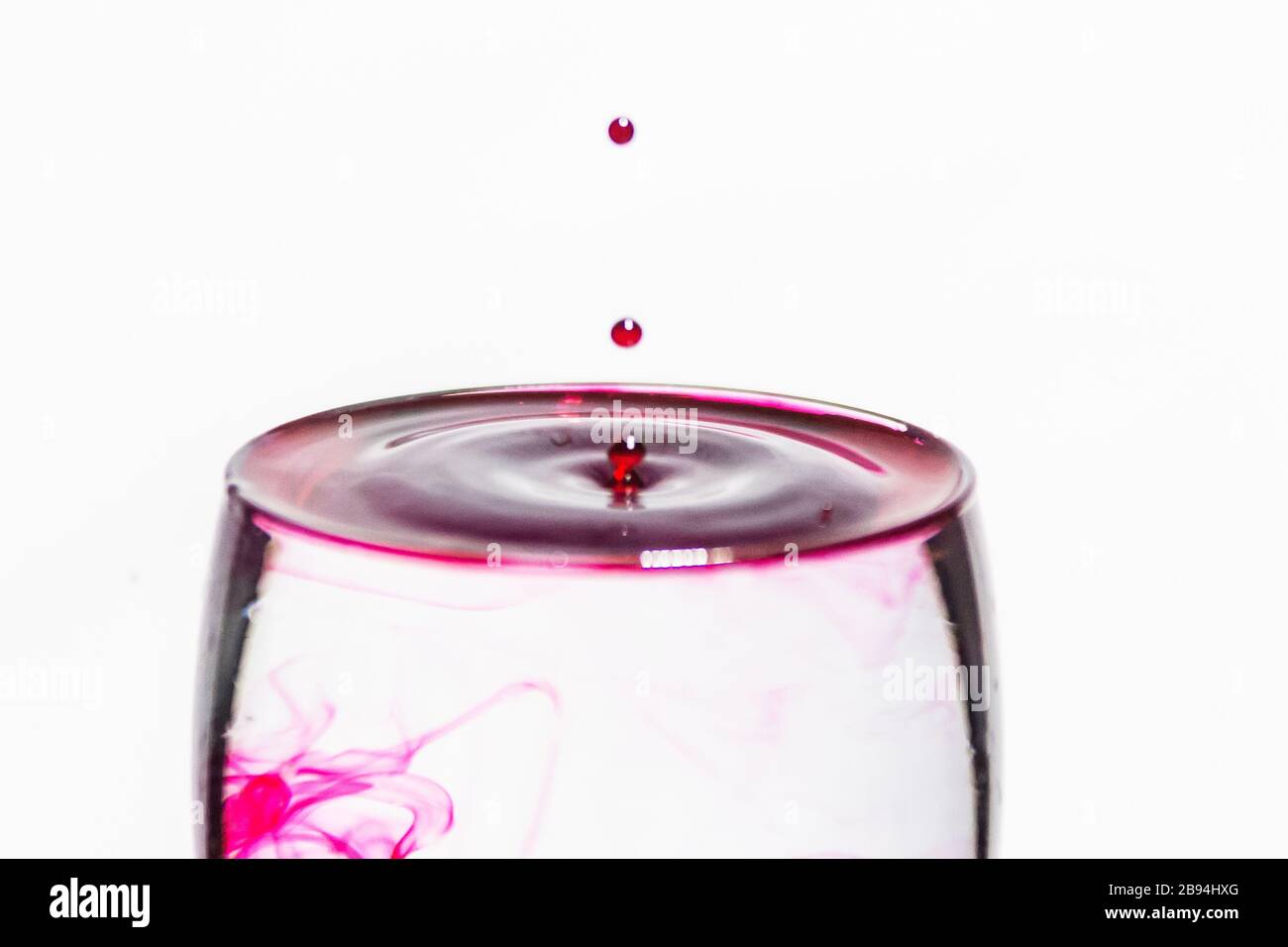 Gocce rosse che spruzzano in un bicchiere d'acqua trasparente Foto Stock