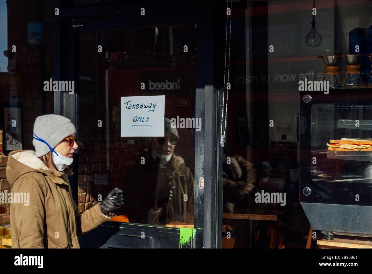 Camberwell, Londra, Regno Unito. 23 marzo 2020. Una donna con un facemask tirato giù entra in un caffè con un segno che dice solo il Takeaway. Credit: Tom Leighton/Alamy Credit: Tom Leighton/Alamy Live News Foto Stock