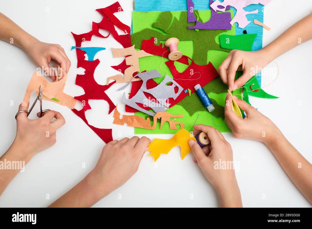 Le mani dei bambini cucire un tessuto di colore diverso. Vista dall'alto sul tavolo bianco Foto Stock