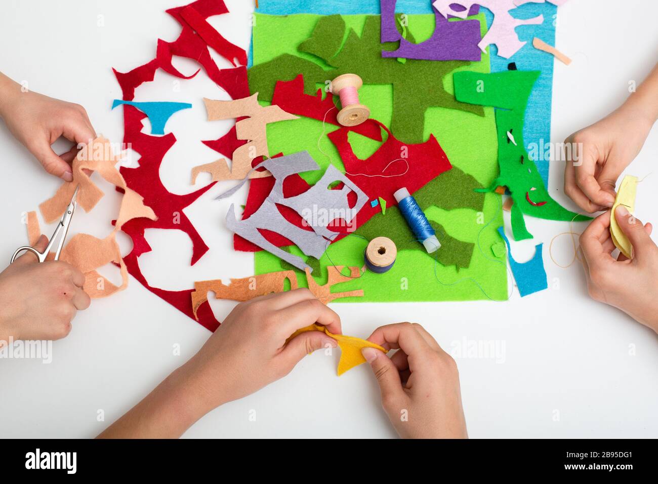 Le mani dei bambini cucire un tessuto di colore diverso sul tavolo bianco. Vista dall'alto Foto Stock