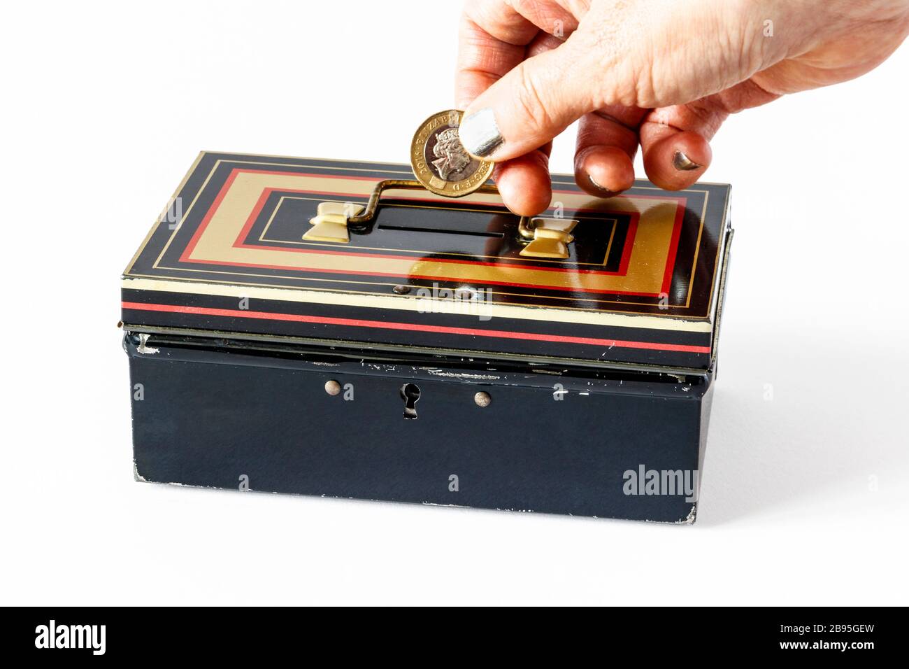 Mano femminile con vernice argentata per unghie che inserisce una moneta da libbra in una cash box giocattolo anni '70 Chad Valley M206 Foto Stock