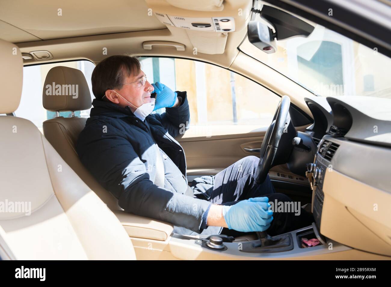 Un uomo che guida in auto con una maschera protettiva e guanti sta parlando al telefono, epidemia di coronavirus. Lavorare durante la quarantena. Rispettare la salute stan Foto Stock
