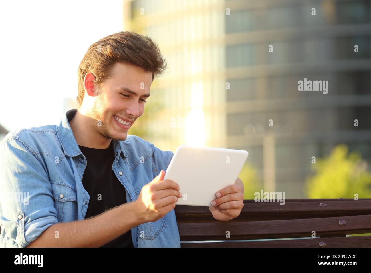 Buon uomo seduto su un banco di lavoro utilizzando un tablet per visualizzare i contenuti online in un parco Foto Stock