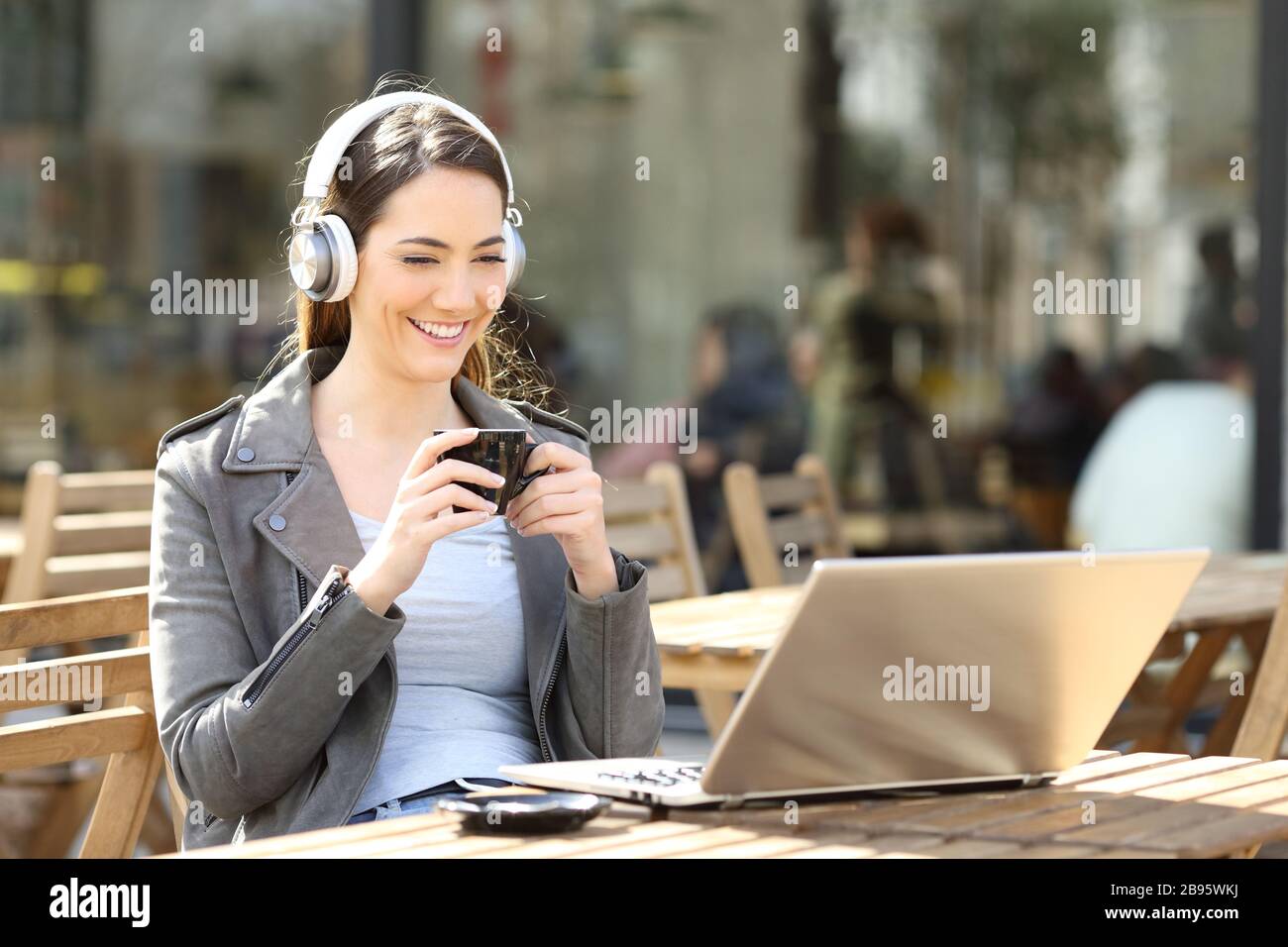 Buona donna che guarda i contenuti video online sul laptop con le cuffie in una terrazza del bar Foto Stock