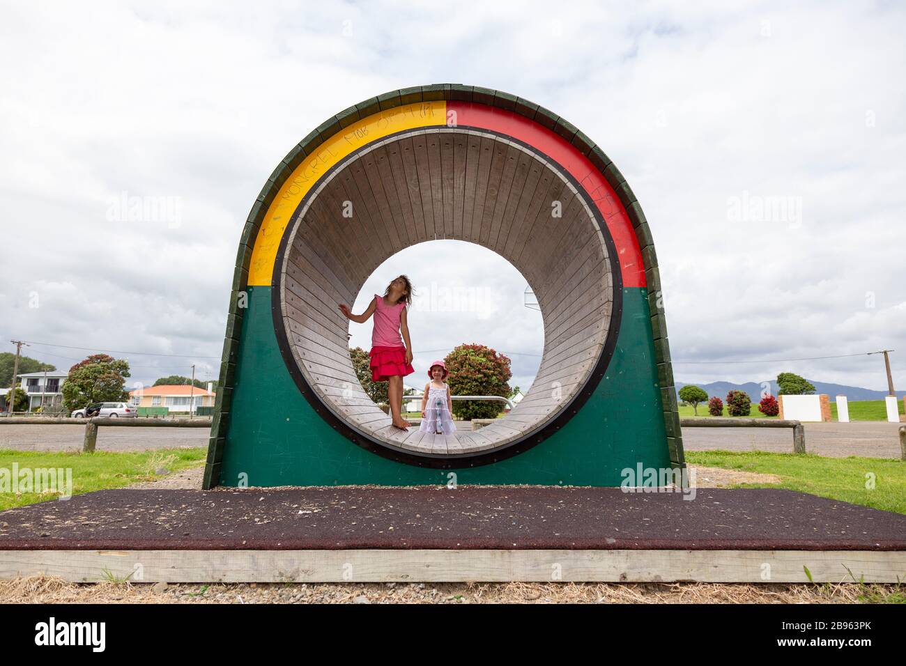 Bambini che esplorano una ruota da ginnastica in un campo da gioco a Opotiki, Nuova Zelanda Foto Stock