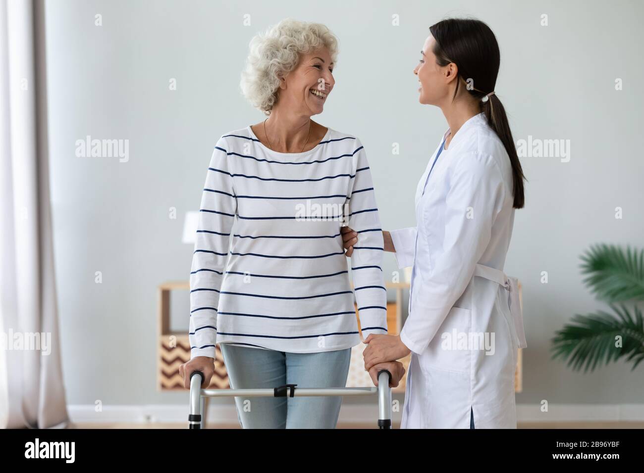 La vecchia signora positiva con il walker parla con l'infermiera premurosa Foto Stock
