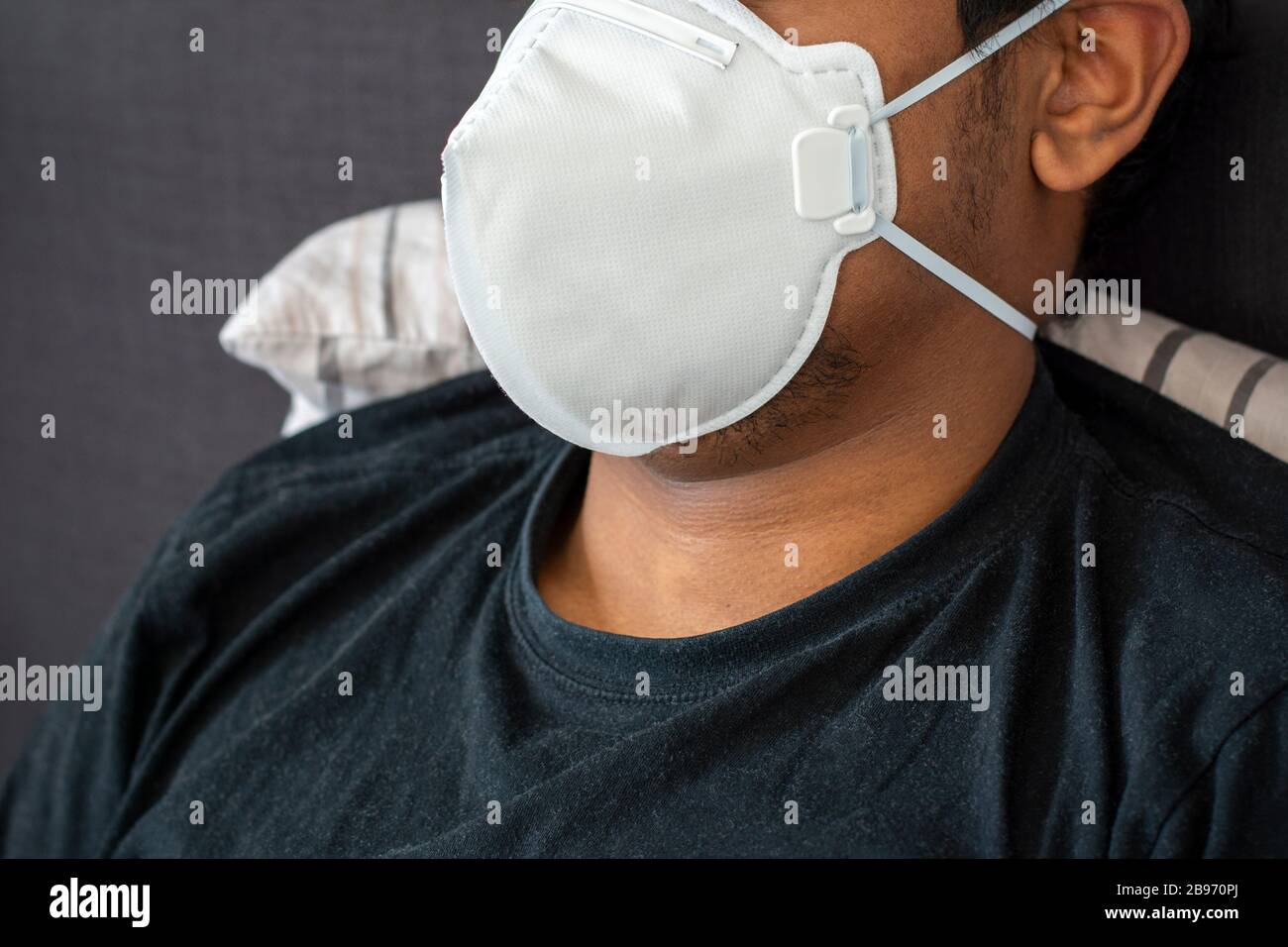 Uomo indiano a letto indossando maschera facciale. Maschera protettiva per bocca chirurgica per polvere medica, respiratore monouso FFP3. Concetto di coronavirus, inquinamento atmosferico Foto Stock