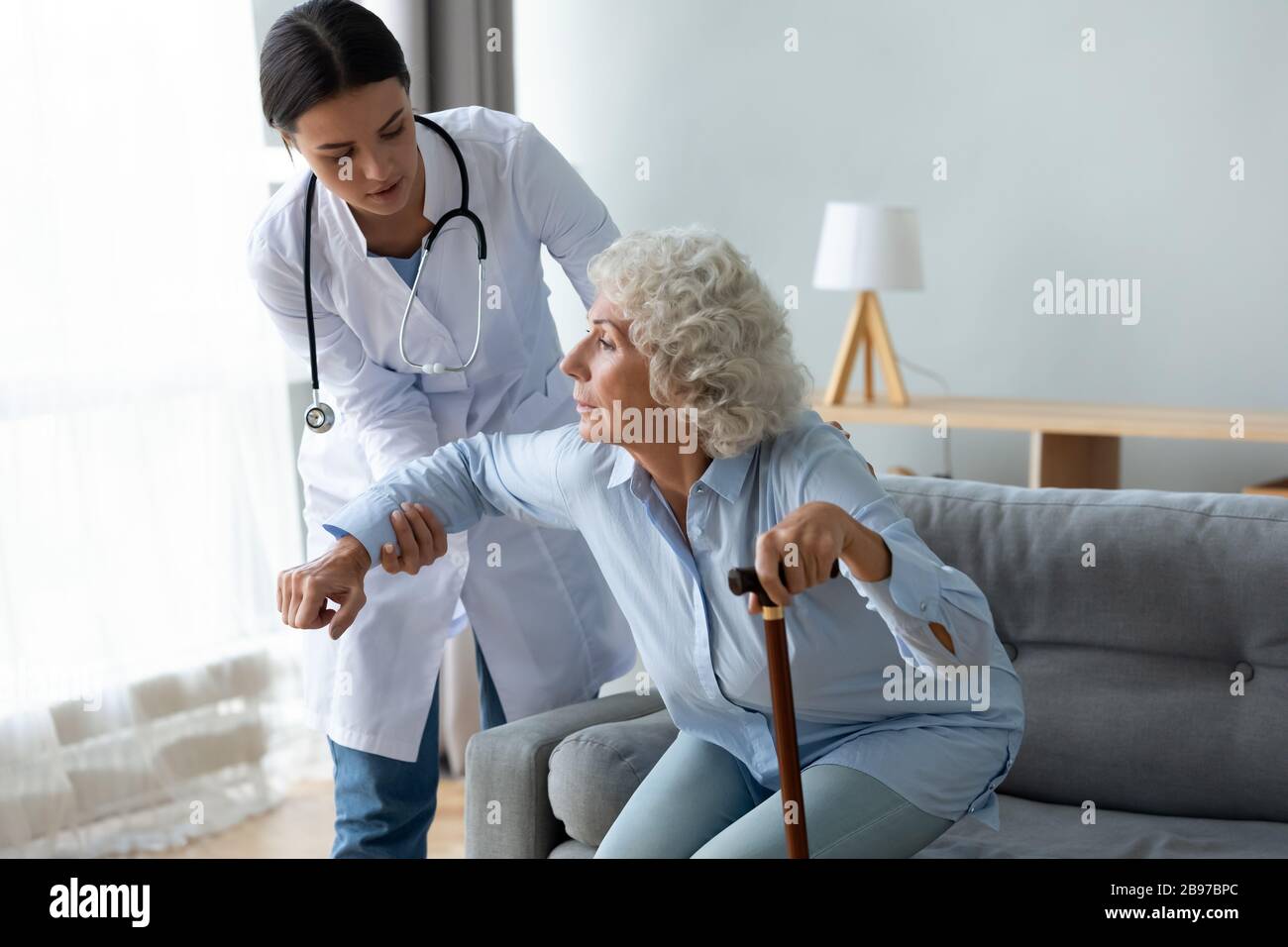 Infermiera femminile aiutare vecchia signora alzarsi dal divano Foto Stock