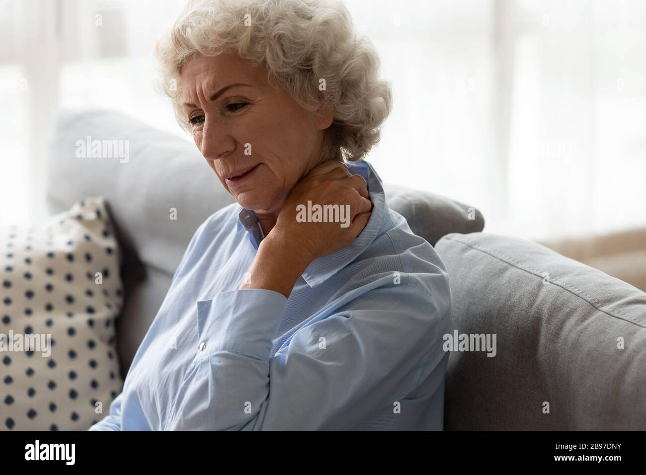 La vecchia signora malata siede sul divano soffrendo dal dolore al collo Foto Stock