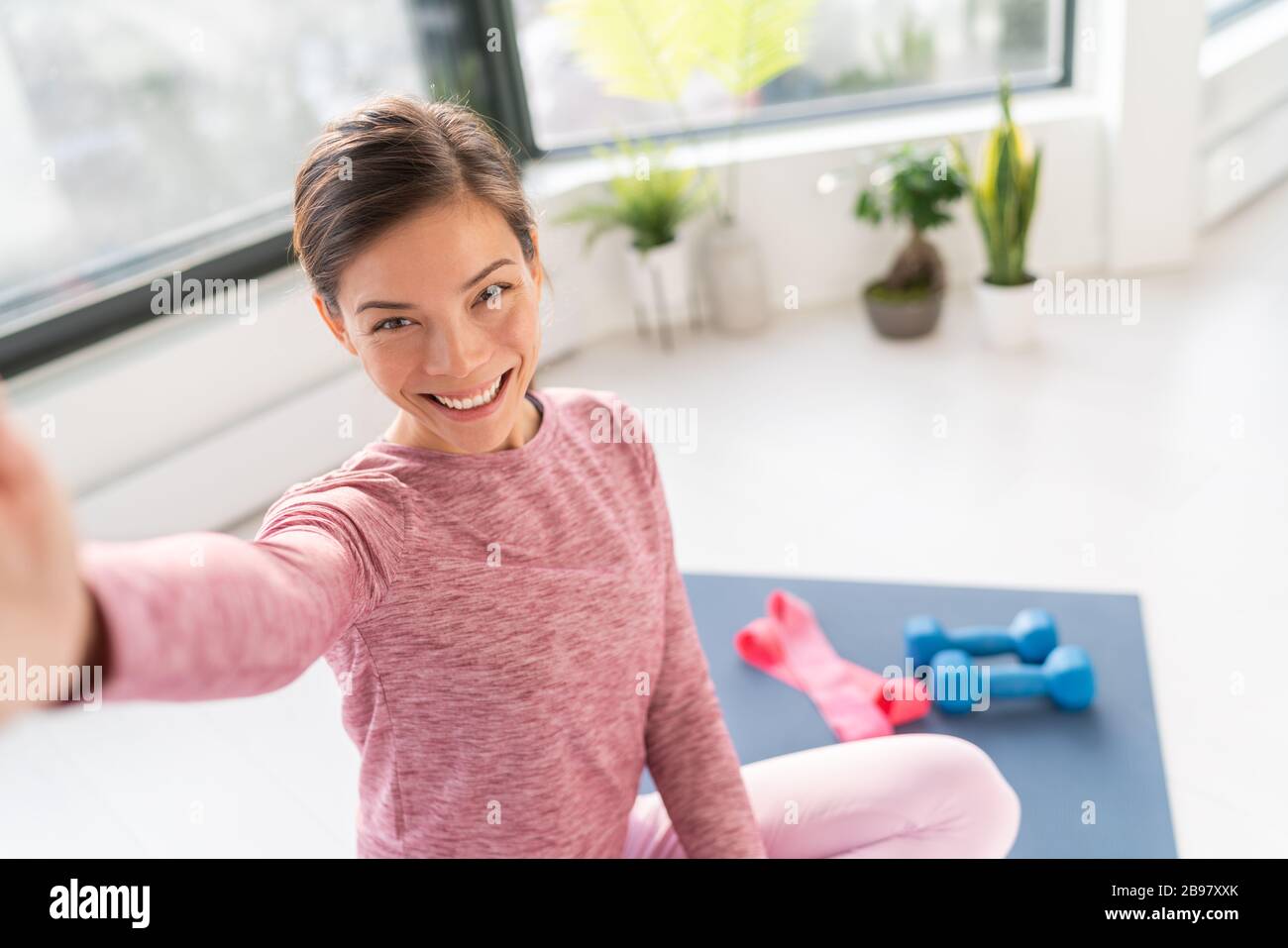 Felice selfie a casa Asian giovane donna sorridente formazione peso corporeo esercizi sul tappetino in soggiorno di prendere appartamento foto del telefono cellulare Foto Stock