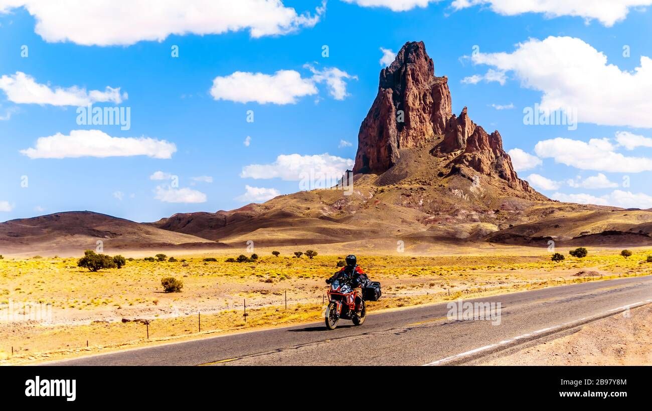 Tour in bici Riders passando le aspre vette di El Capitan e Agathla Peak torreggiando sul paesaggio desertico a sud della Monument Valley sulla US 163 Foto Stock