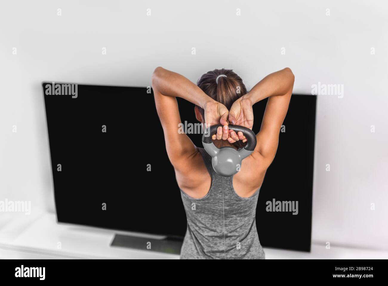 Home esercizio di forza allenamento allenamento overhead triceps extension muscoli esercizi donna che guarda online tv fitness class live streaming a casa Foto Stock