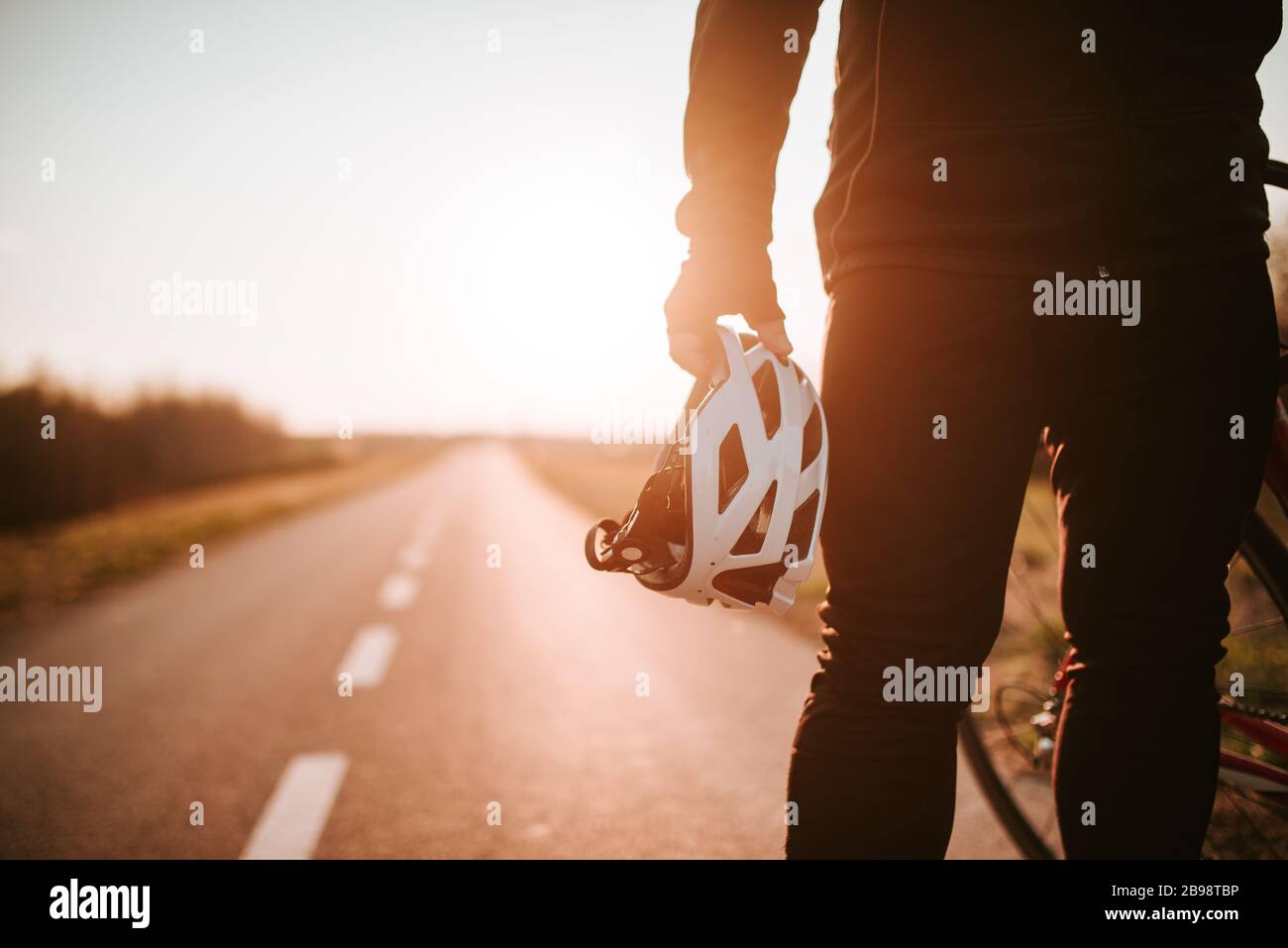 Il ciclista tiene il casco in mano e si alza sulla strada Foto Stock