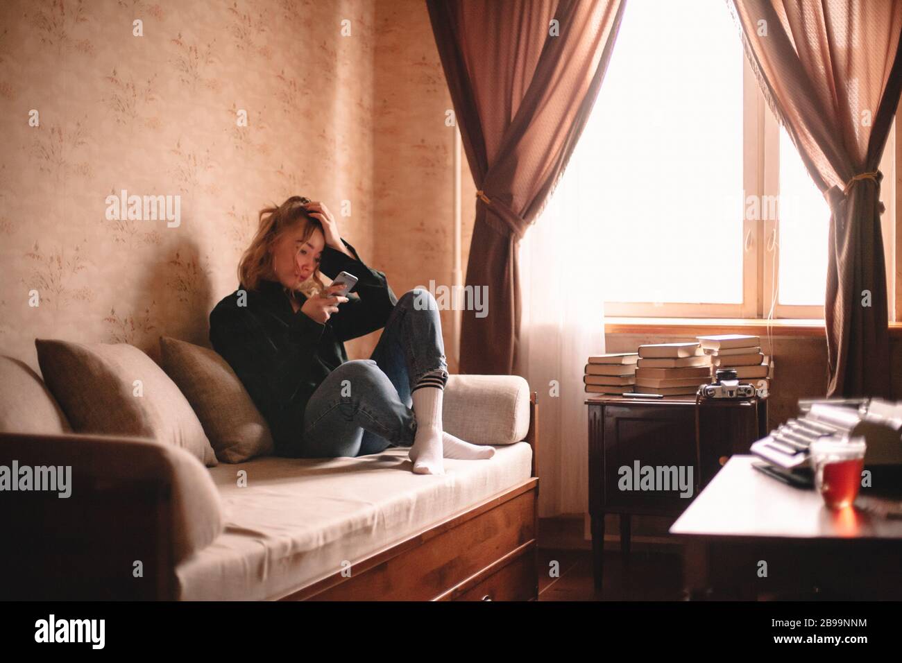 Giovane triste donna stressata utilizzando smartphone mentre si siede sul divano a casa Foto Stock