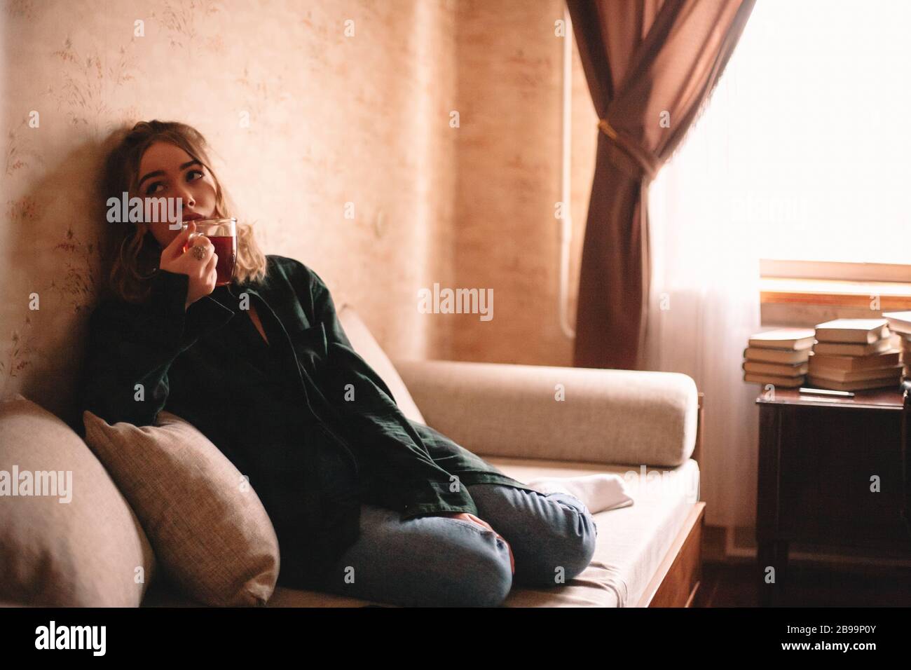 Giovane annoiato donna bere il tè mentre siede sul divano nel soggiorno a casa Foto Stock