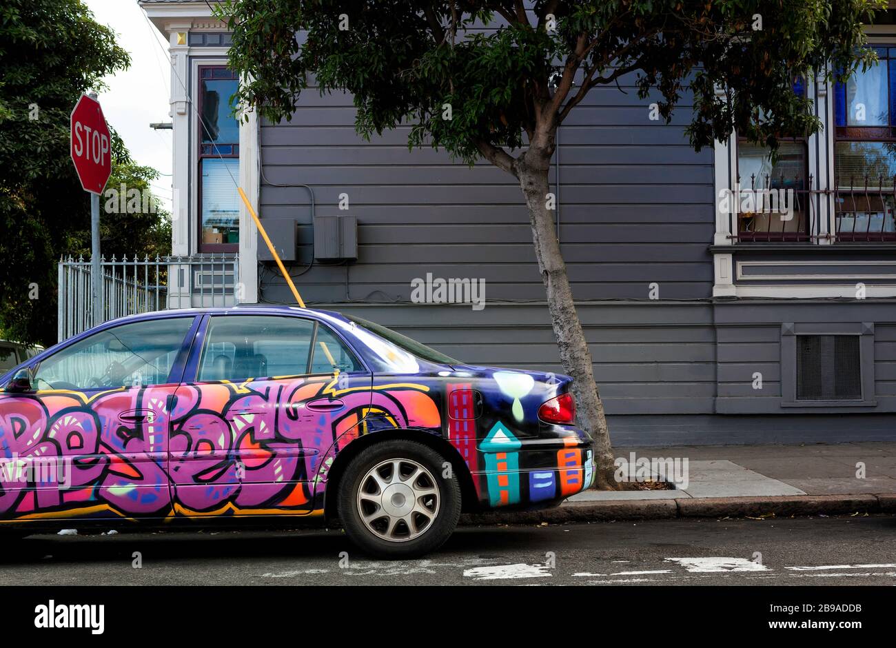 Un'auto coperta da graffiti aggiunge colore a una strada nel Mission District, San Francisco, California, Stati Uniti, Nord America Foto Stock