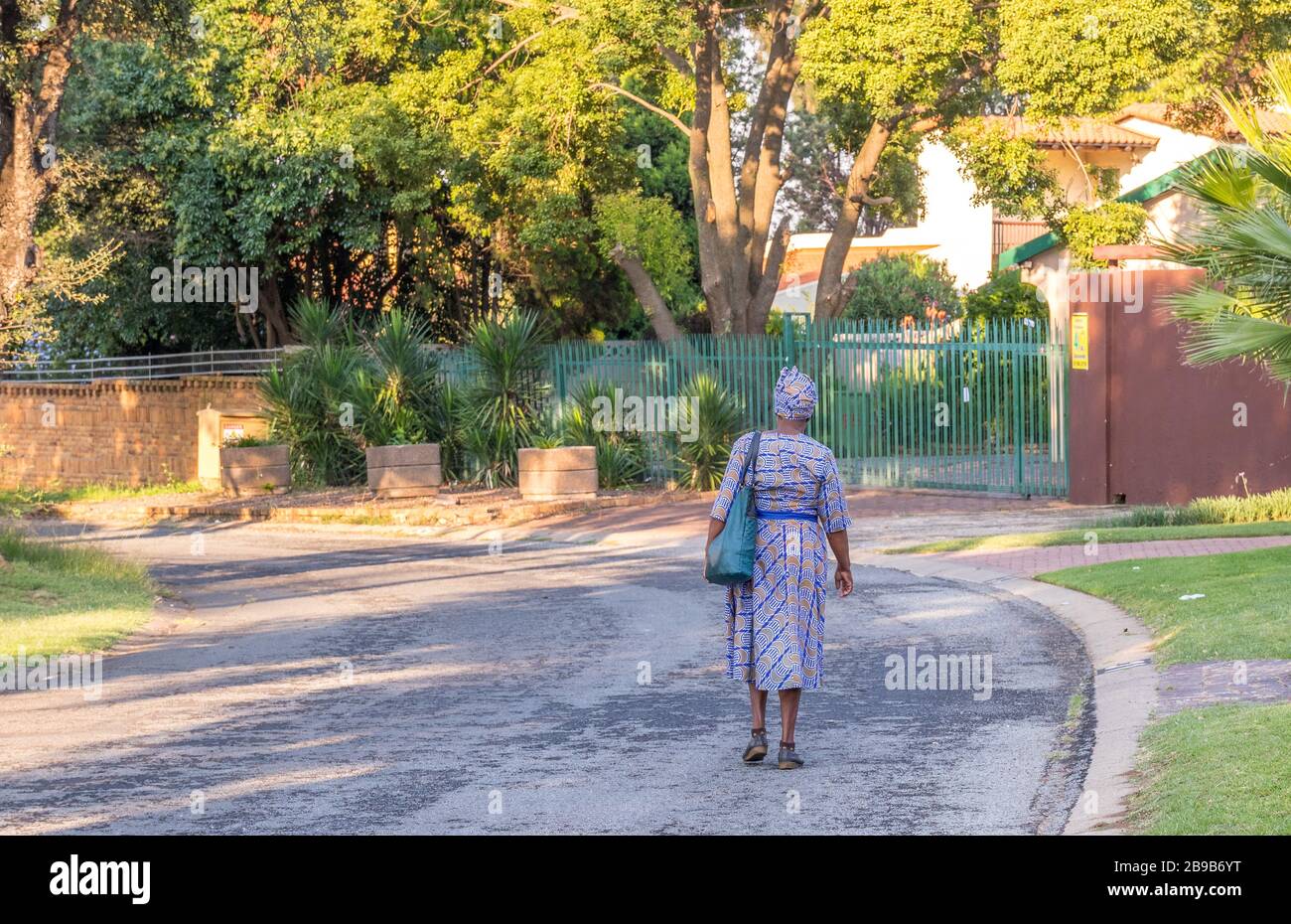 Alberton, Sud Africa - una donna nera africana single anziana cammina da sola in un'immagine di strada residenziale deserta in formato orizzontale Foto Stock