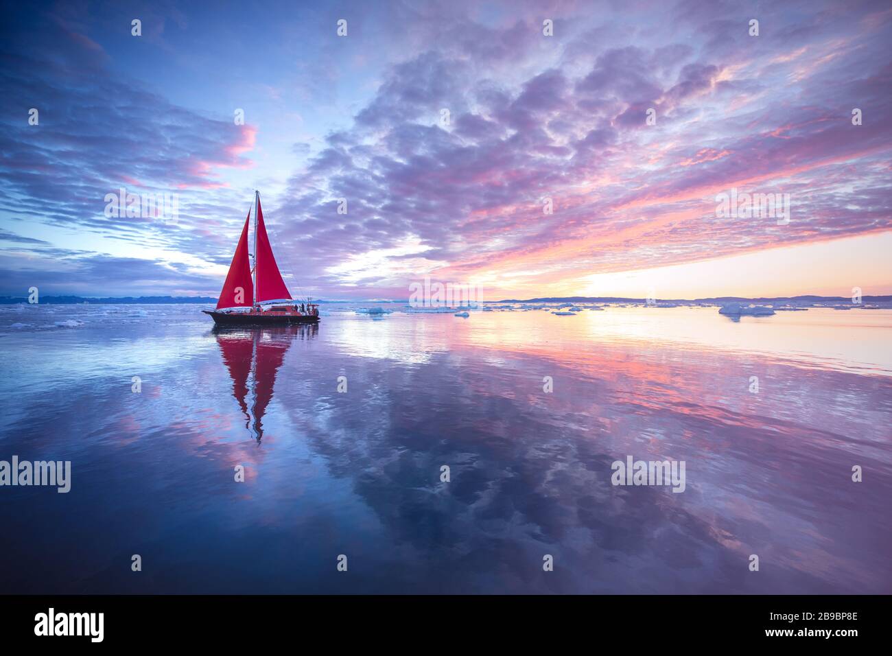 Barca a vela con vele rosse che naviga tra le ormeggi di ghiaccio durante la stagione solare di mezzanotte. Disko Bay, Groenlandia. Foto Stock