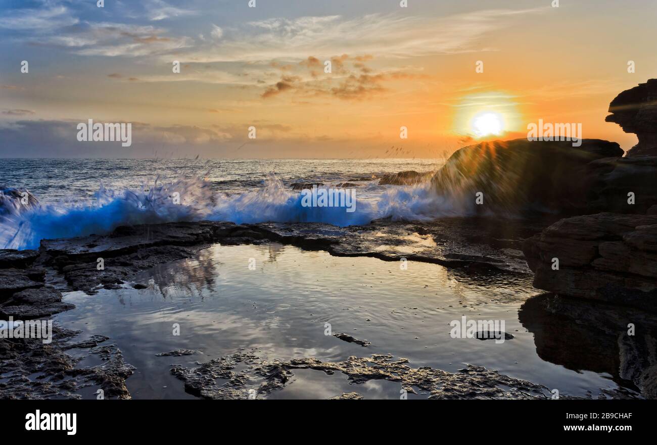 Caldo sole in ascesa sull'orizzonte e rocce di arenaria di Turimetta testa di Sydney Northern Beaches. Foto Stock