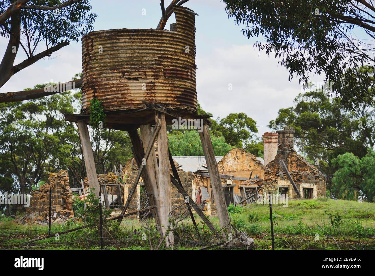 Old Stone Farmhouse in riparazione con Rusty Old Water Tank sotto albero Foto Stock