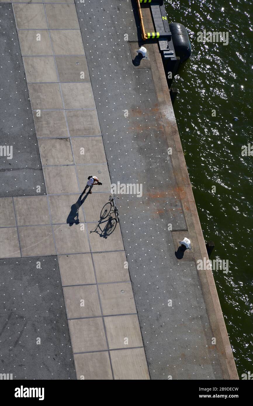 Vista dall'occhio degli uccelli sul molo con l'uomo da solo e la bicicletta che lancia lunghe ombre su un interessante modello del molo di cemento Foto Stock